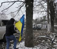 A man takes a Ukrainian national flag swinging from a tree as he walks near a destroyed accommodation building by a checkpoint in Brovary, outside Kyiv, Ukraine, Tuesday, March 1, 2022. Russian shelling pounded civilian targets in Ukraine's second-largest city Tuesday and a 40-mile convoy of tanks and other vehicles threatened the capital — tactics Ukraine's embattled president said were designed to force him into concessions in Europe's largest ground war in generations. (AP Photo/Efrem Lukatsky)