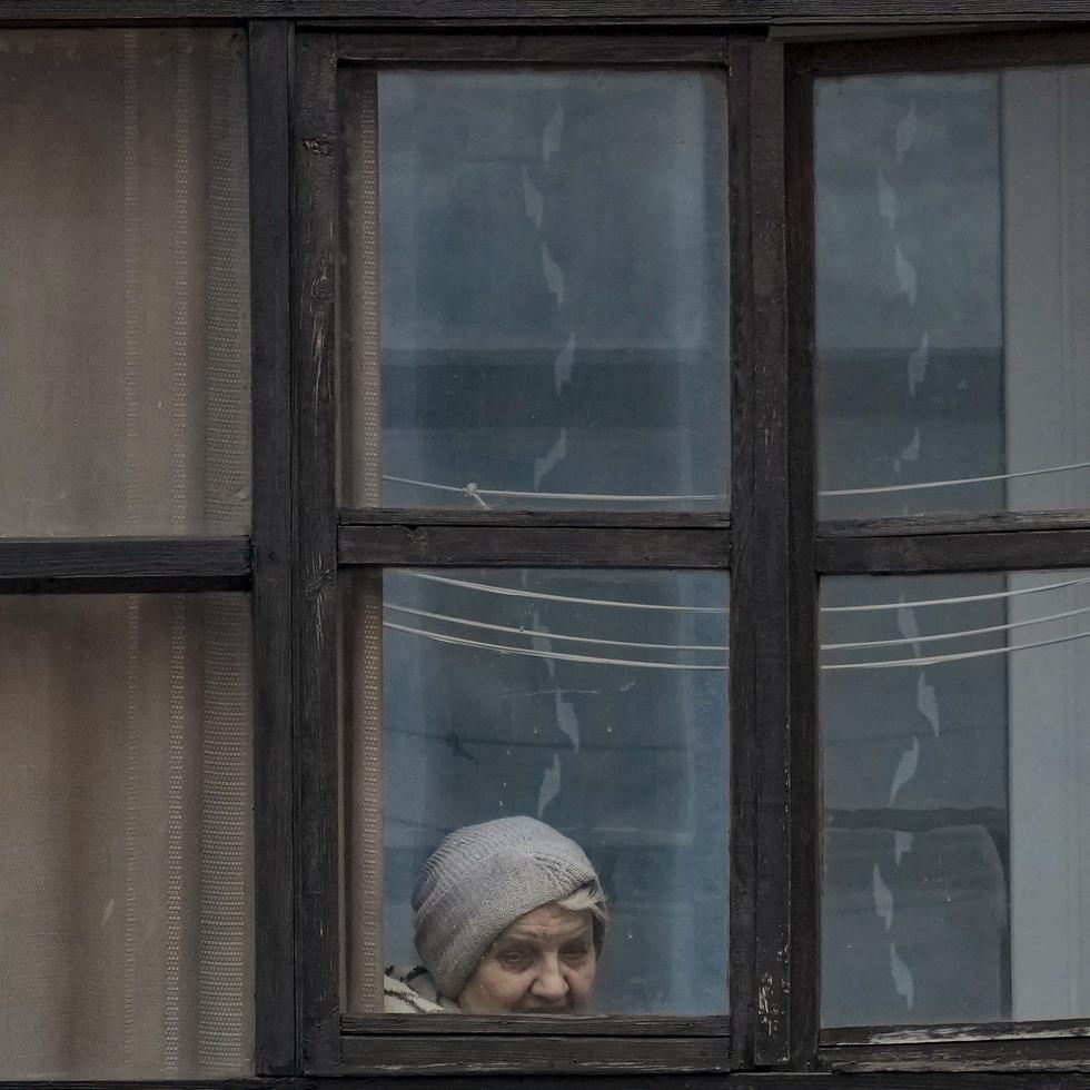 Una mujer mira por la ventana de una vivienda en Sievierodonetsk, en la región de Luhansk, en el este de Ucrania, el 18 de febrero de 2022. (AP Foto/Vadim Ghirda)