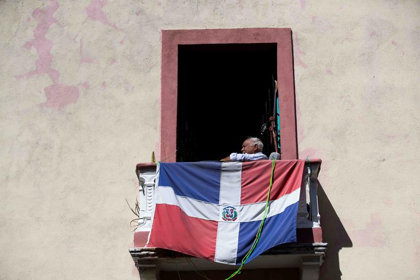 Un anciano observa desde su balcón, donde tiene colgada una bandera dominicana. (EFE)