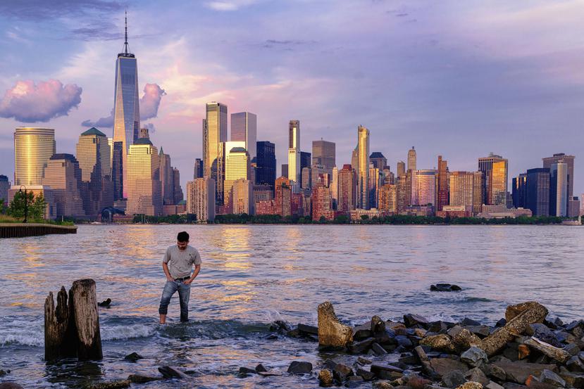 Un hombre comprueba dónde pisa mientras camina por el agua en el Canal Morris en Jersey, Nueva Jersey, mientras se pone el sol con Manhattan de fondo, el 31 de mayo de 2022. (AP Foto/J. David Ake, Archivo)