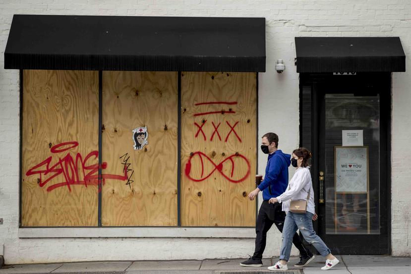 Unas personas con mascarillas caminan frente a una tienda cerrada en Washington D.C. (AP)