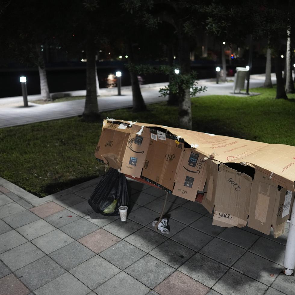 Una persona duerme dentro de un refugio improvisado en el banco de un parque en el centro de Miami.