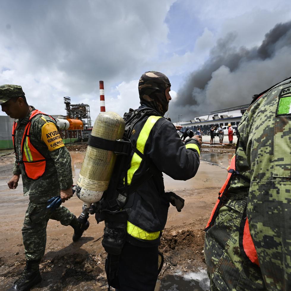A Cuban firefighter stands between Mexican soldiers as they work to put out a deadly fire at a large oil storage facility in Matanzas, Cuba, Tuesday, Aug. 9, 2022. The fire was triggered when lighting struck one of the facility's eight tanks late Friday, Aug. 5th. (Yamil Lage, Pool photo via AP)