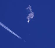 Fotografía proporcionada por Chad Fish de los restos de un globo cayendo sobre el océano Atlántico frente a la costa de Carolina del Sur (arriba a la derecha), mientras abajo se observa un avión de combate y su estela, el sábado 4 de febrero de 2023.