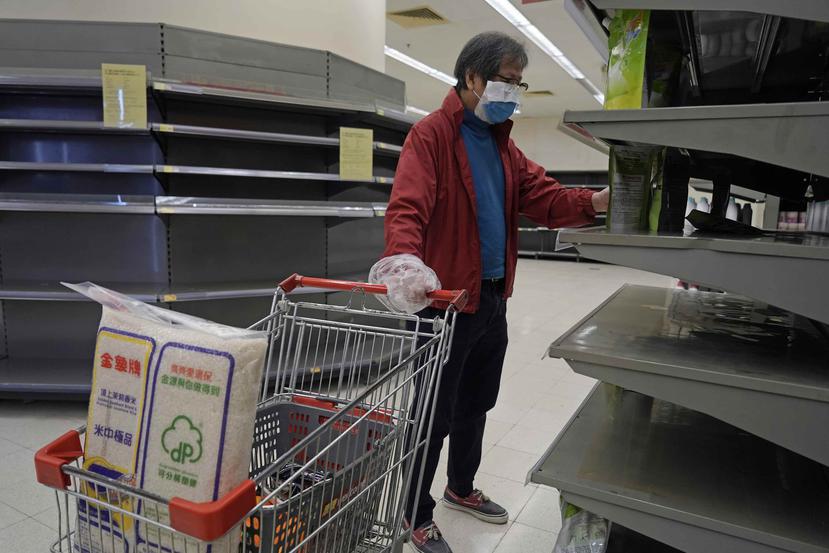 Un hombre portando un cubrebocas y bolsas de plástico como guantes revisa las estanterías vacías en busca de papel higiénico en un supermercado en Hong Kong. (AP/Kin Cheung)
