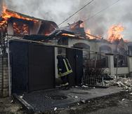 Un bombero se para en una casa en llamas golpeada por los bombardeos rusos en Kherson, Ucrania, en la víspera de Navidad ortodoxa el viernes 6 de enero de 2023.