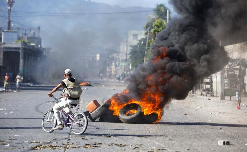 Un ciclista pasa cerca de gomas encendidas por manifestantes que exigen saber cómo las administraciones actuales y pasadas de Haití utilizaron los fondos de un acuerdo petrolero con Venezuela. (EFE)