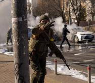 Ukrainian soldiers take positions outside a military facility as two cars burn, in a street in Kyiv, Ukraine, Saturday, Feb. 26, 2022. Russian troops stormed toward Ukraine's capital Saturday, and street fighting broke out as city officials urged residents to take shelter. (AP Photo/Emilio Morenatti)