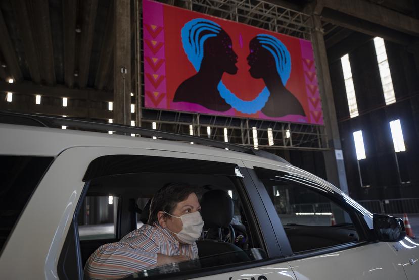 Una mujer con una mascarilla para protegerse del coronavirus observa una exposición artística desde un automóvil el viernes 24 de julio de 2020, en una nave donde están expuestas pinturas y fotografías, en Sao Paulo, Brasil. (AP Foto/André Penner)