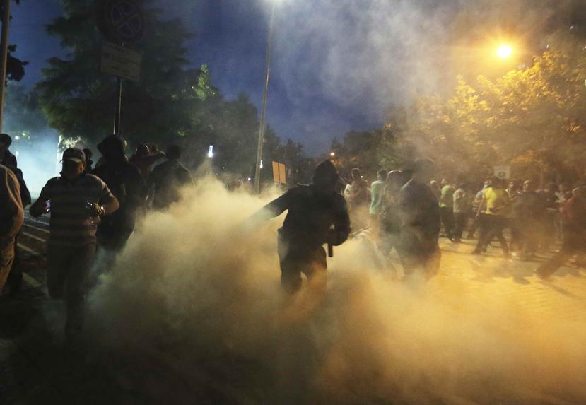 Manifestantes pasan por una nube de gas lacrimógeno durante una protesta contra el gobierno en Tirana. (AP/Hektor Pustina)