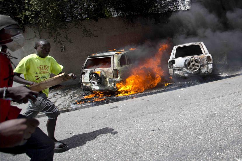 Personas corren luego que protestantes prendieron fuego a varios automóbiles durante los disturbios en Haití por el alza en el precio de los combustibles. (AP / Dieu Nalio Chery)