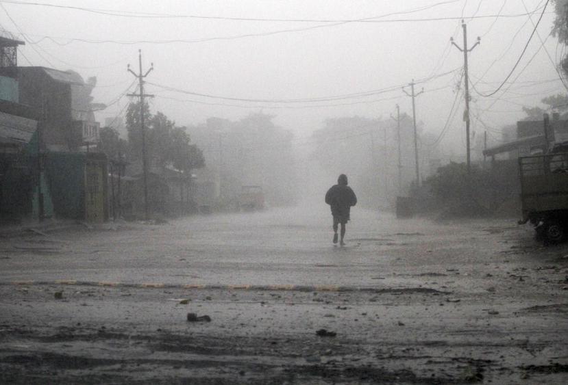 Un hombre camina por una calle en medio de fuertes lluvias y vientos provocados por el ciclón Titli, cerca de Gopalpur, en India. (AP)