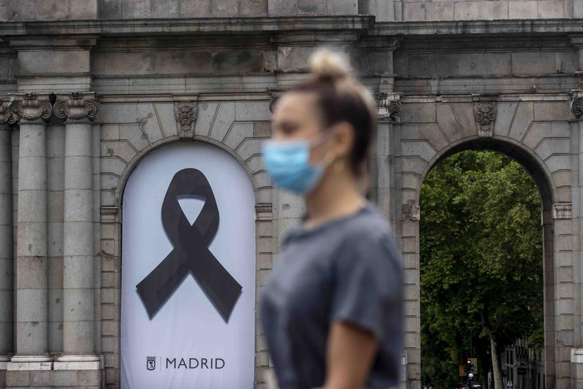 Una mujer camina con mascarilla frente a un lazo negro en honor a los fallecidos por COVID-19 en Madrid. (AP)