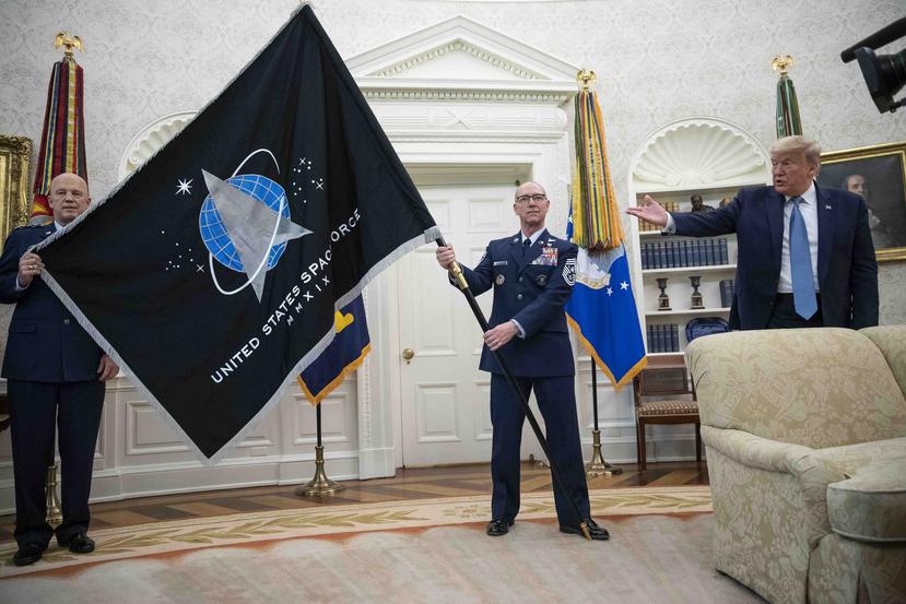 El general John “Jay” Raymond, titular del Comando Espacial de Estados Unidos, a la izquierda, y el sargento maestre superior Roger Towberman, a la derecha, sostienen la bandera de la Fuerza Espacial para mostrársela al presidente Donald Trump el viernes
