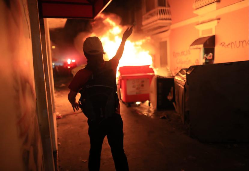 Un manifestante lanza un objeto mientras arden en fuego varios contenedores de plástico en la calle Fortaleza.
