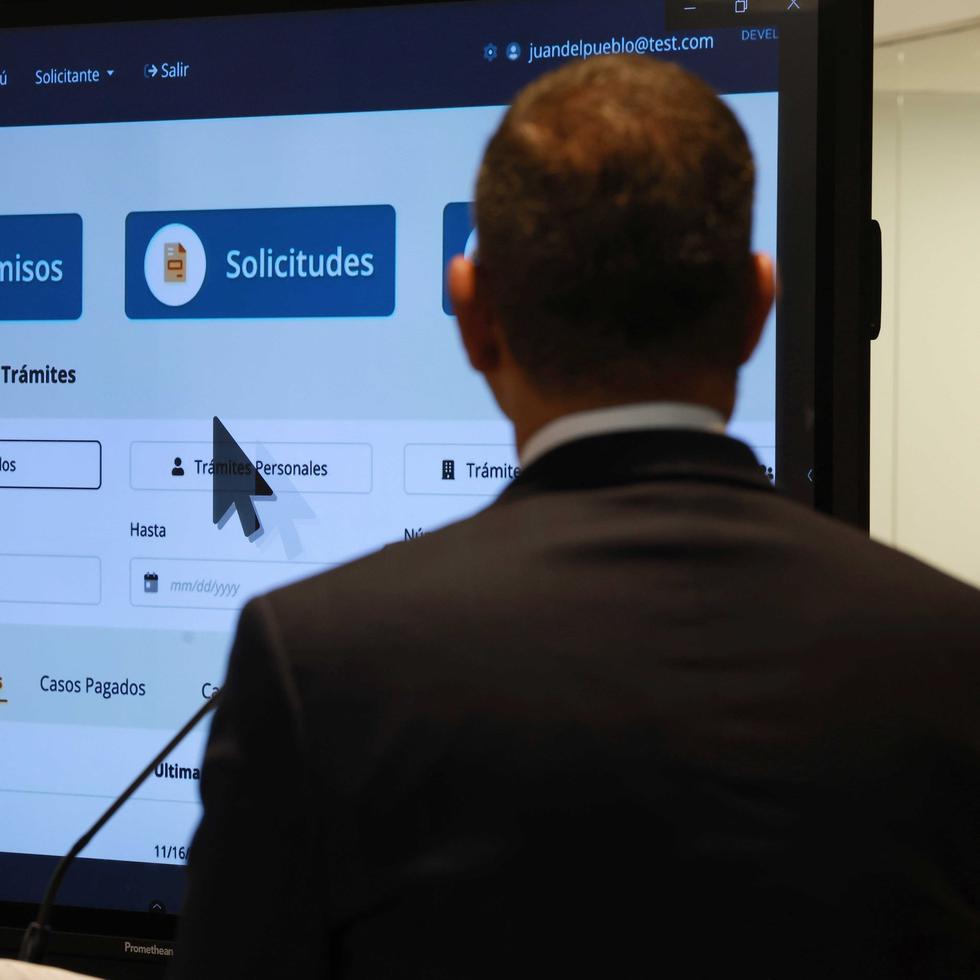 En primer plano, la silueta del gobernador Pedro Pierluisi, quien observa la pantalla donde se muestra la nueva plataforma para tramitar permisos a través de la Oficina de Gerencia de Permisos.
