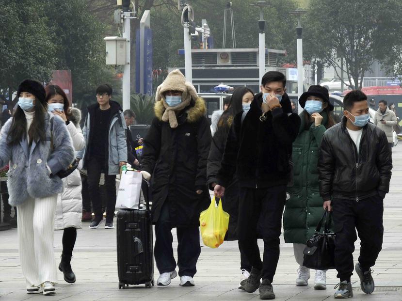 Viajeros usan mascarillas mientras caminan afuera de una estación de tren en Yichang, en la provincia de Hubei, en el sur de China. (AP)