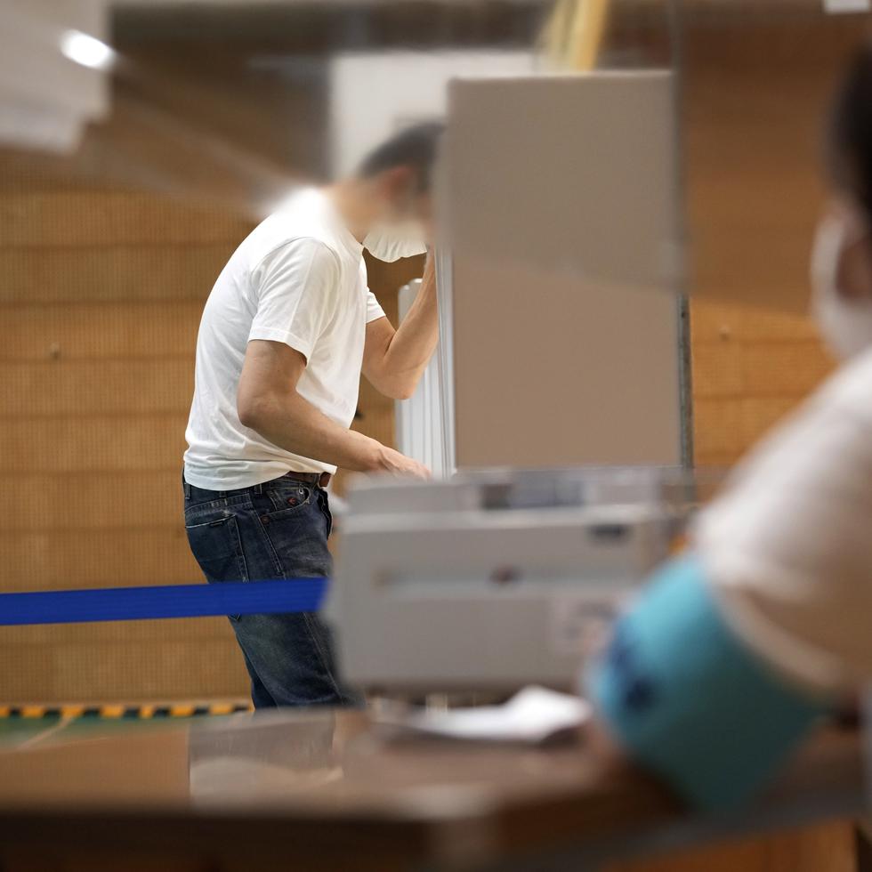 Una trabajadora de la administración electoral local mira mientras un votante prepara su boleta para los comicios parlamentarios en una casilla electoral en Tokio.