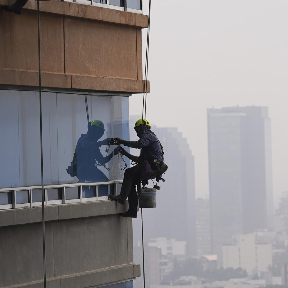 Limpiadores de ventanas están suspendidos de cuerdas en un edificio de apartamentos de gran altura en la Ciudad de México, el miércoles 13 de diciembre de 2023. (AP Foto/Marco Ugarte)