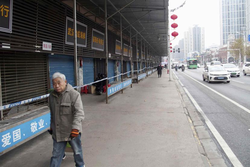 Un hombre pasa frente al Mercado Huanan de Mariscos, que permanece cerrado tras un brote de coronavirus ligado al lugar, en Wuhan, China. (AP)