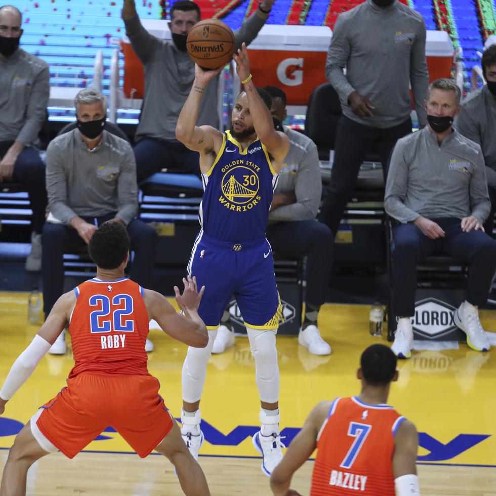 Stephen Curry (centro) dispara un triple contra Isaiah Roby, del Oklahoma City Thunder, durante la primera mitad del juego de ayer.