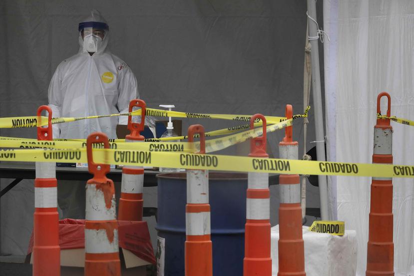 Un empleado de salud cubierto con equipo protector por la pandemia del coronavirus aguarda en un punto de revisión y diagnóstico para conductores en el estacionamiento del Gillette Stadium. (AP)