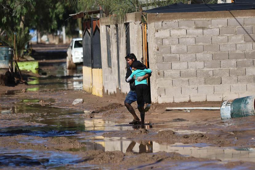 Un hombre cruza con su hija por una calle inundada debido a un temporal de lluvia que ya ha dejado dos personas fallecidas y más de 100 damnificadas en Chile. (EFE / José Ulloa)