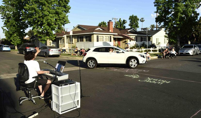 En esta fotografía del 9 de mayo de 2020 el músico Adam Chester, izquierda, saluda a un vecino que pasa en su auto mientras interpreta su concierto semanal en su barrio en la sección de Sherman Oaks en Los Angeles. Chester suele ser un sustituto de Elton
