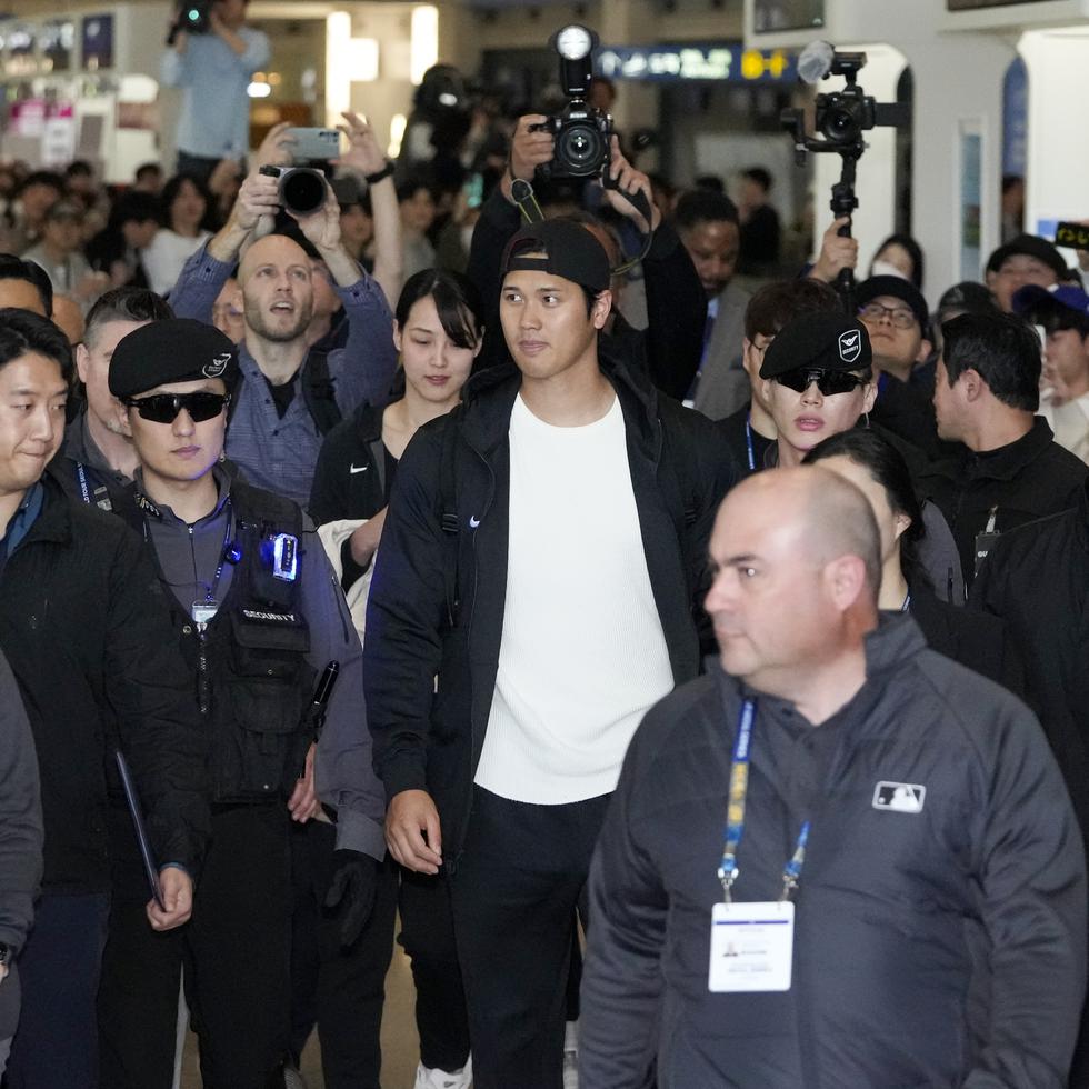 Shohei Ohtani, al centro, camina con su esposa Mamiko Tanaka por el Aeropuerto Internacional Incheon, de Corea del Sur, roeados de personal de seguridad.