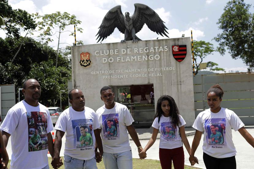 Familiares de los jóvenes futbolistas que fallecieron hace un año en un incendio que arrasó con un centro de entrenamiento del equipo brasileño de Flamengo, rezan afuera del complejo en Río de Janeiro. (AP / Silvia Izquierdo)