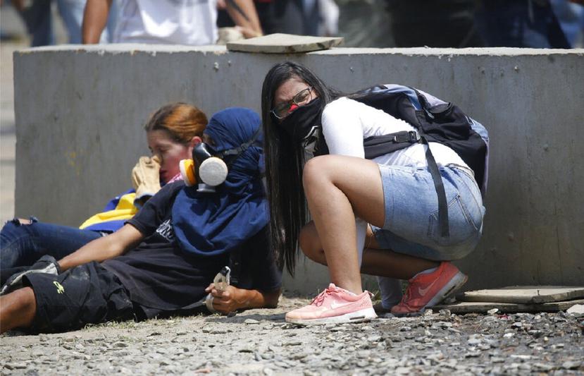 Jóvenes venezolanos se cubren de los gases lacrimógenos, durante un enfrentamiento con la Policía, en Caracas. (AP)
