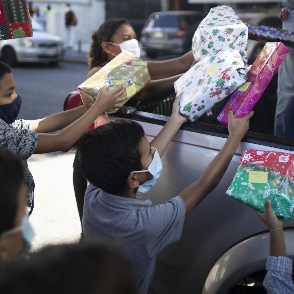 Los niños reciben regalos de Navidad donados por el grupo de voluntarios "Un Juguete, Una Buena Noticia" desde la parte trasera de una camioneta en Caracas, Venezuela, el viernes 18 de diciembre de 2020. (AP Foto/Ariana Cubillos)
