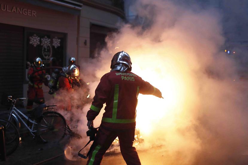 Bomberos intentan extinguir el fuego de un vehículo incendiado por manifestantes durante un enfrentamiento con policías antidisturbios en París, el sábado 8 de diciembre de 2018. (AP/Thibault Camus)