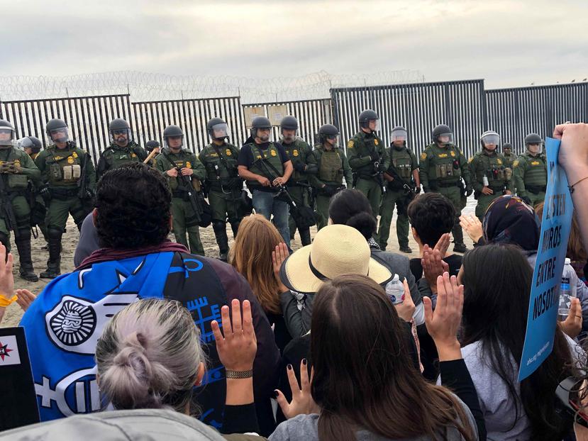 Un grupo de inmigrantes se concentra frente a miembros del Servicio de Protección Federal de México (FPS), a metros del muro fronterizo entre Tijuana (México) y San Diego (California, EE.UU.). (EFE)