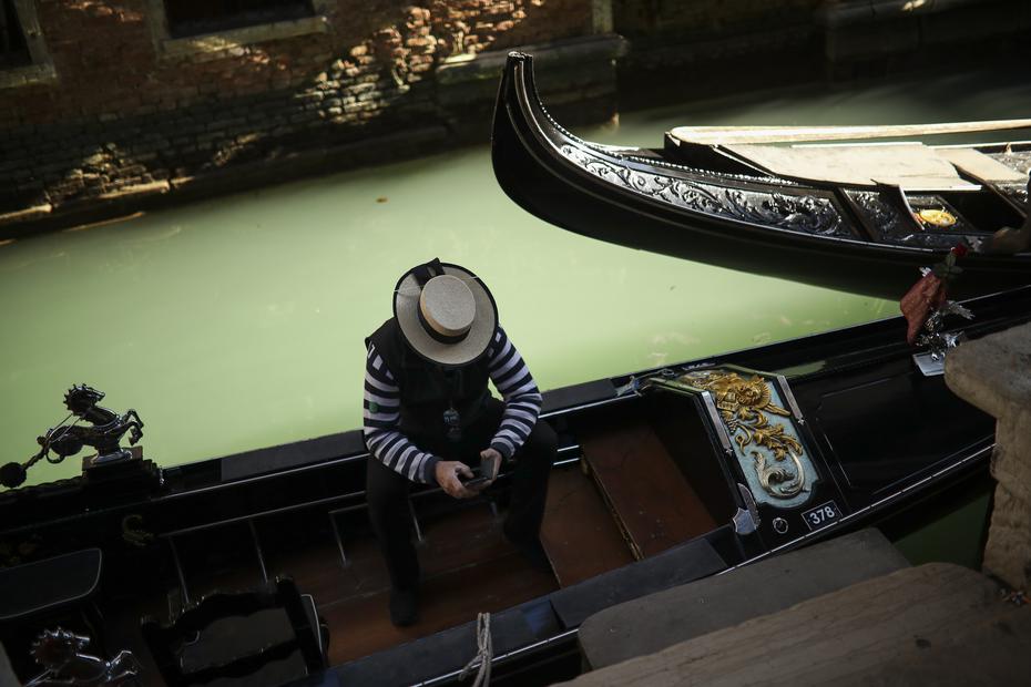 Un gondolero mira su teléfono mientras espera ser contratado por alguno de los pocos turistas que visitan Venecia desde el estallido de un brote de coronavirus. Foto del 28 de febrero del 2020.