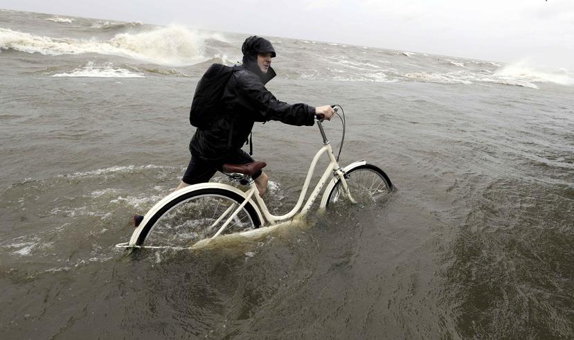 Tyler Holland guía su bicicleta mientras el viento de la tormenta tropical Barry empuja el agua del lago Pontchartrain sobre un dique. (AP)
