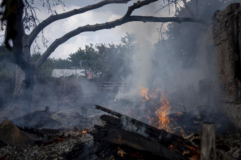 Un hombre intenta apagar un incendio en el patio de un vecino cuya residencia fue destruída por un ataque ruso en Mykolaiv.