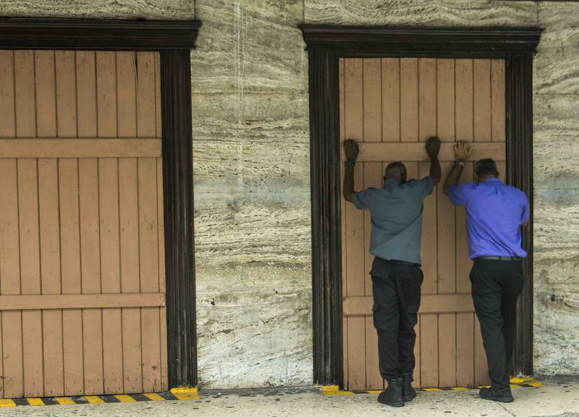 Unas personas cubren con madera la fachada de una farmacia mientras se preparan para la llegada de la tormenta tropical Dorian, en Barbados. (AP/Chris Brandis)