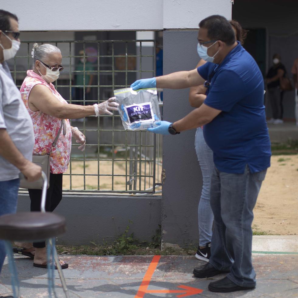 Un empleado del Municipio de Cataño entega un kit con desinfectante de manos y mascarillas a una mujer que aguarda en fila para comprar mariscos.