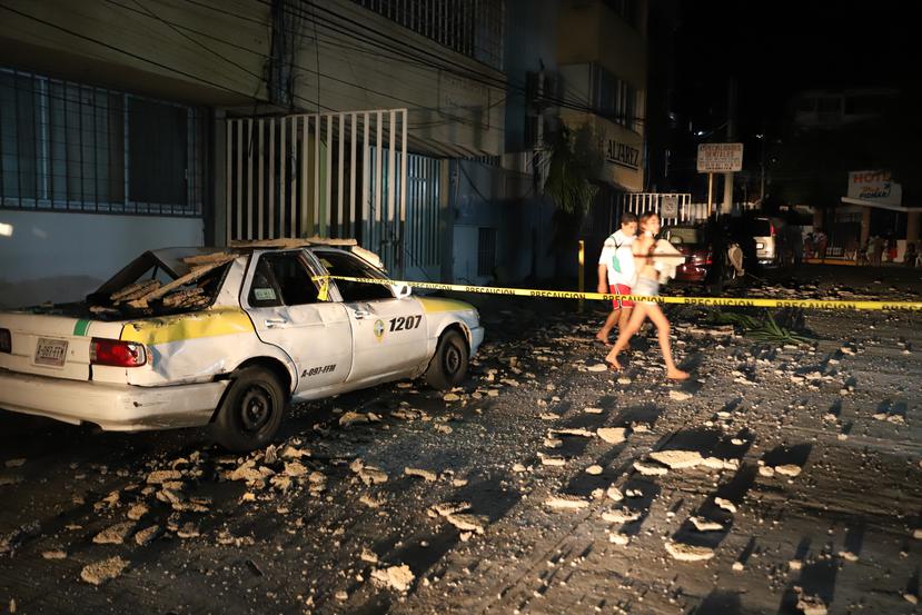 Una pareja pasa junto a un taxi que resultó dañado por la caída de escombros después de un fuerte terremoto en Acapulco, México, el martes 7 de septiembre de 2021.