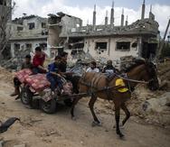 Palestinos en un carro tirado por un caballo y cargado con sus pertenencias pasan junto a viviendas destruidas, a las que regresan tras un cese de fuego después de 11 días de guerra entre Hamás e Israel.