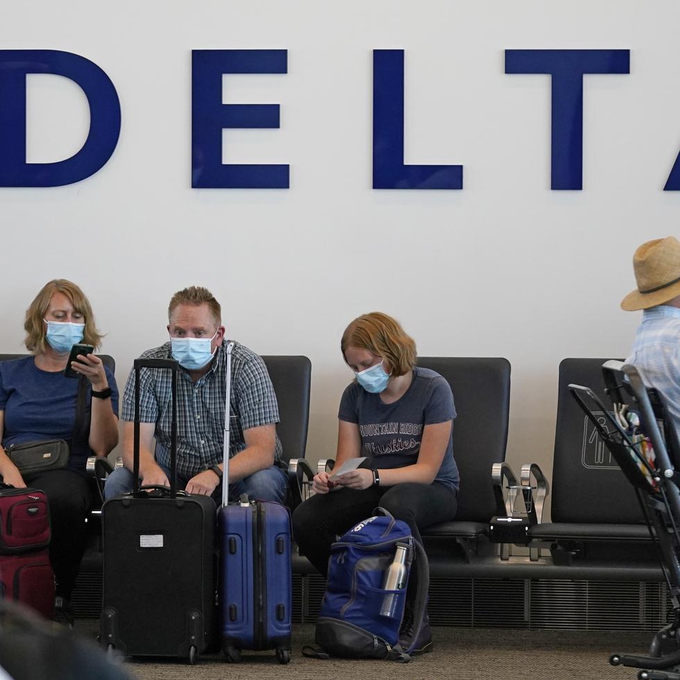 Personas están sentadas bajo el cartel de Delta en el Aeropuerto Internacional de Salt Lake City.