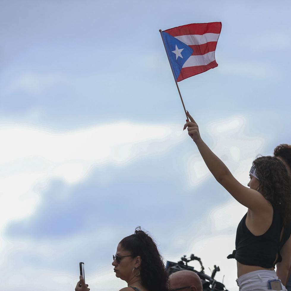 Una manifestante alza la bandera de Puerto Rico en el inicio de la marcha desde el Capitolio.