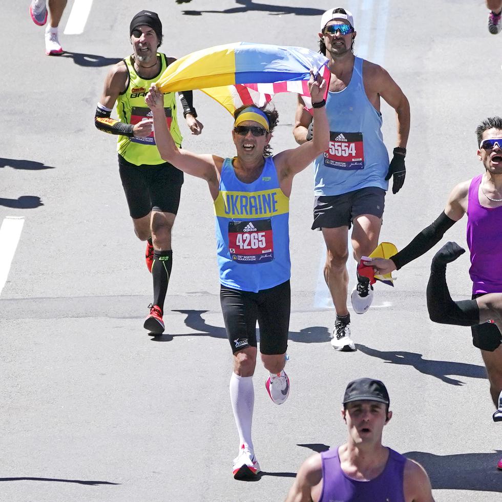 Vestido con una camiseta de Ucrania, un corredor alza una bandera combinada de Ucrania y Estados Unidos mientras se acerca a la línea de mete del Maratón de Boston.