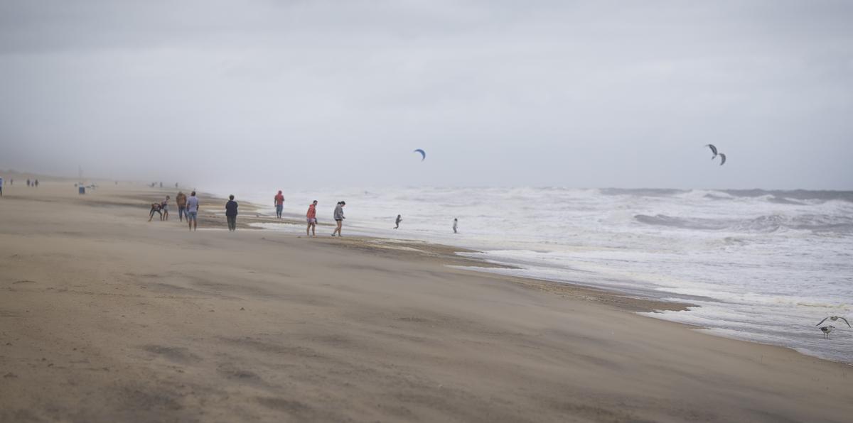 Un grupo de bañistas mira a gente haciendo kitesurf entre las olas provocadas por la tormenta tropical Ophelia, el sábado 23 de septiembre de 2023 en Virginia Beach, Virginia. (AP Foto/John C. Clark)