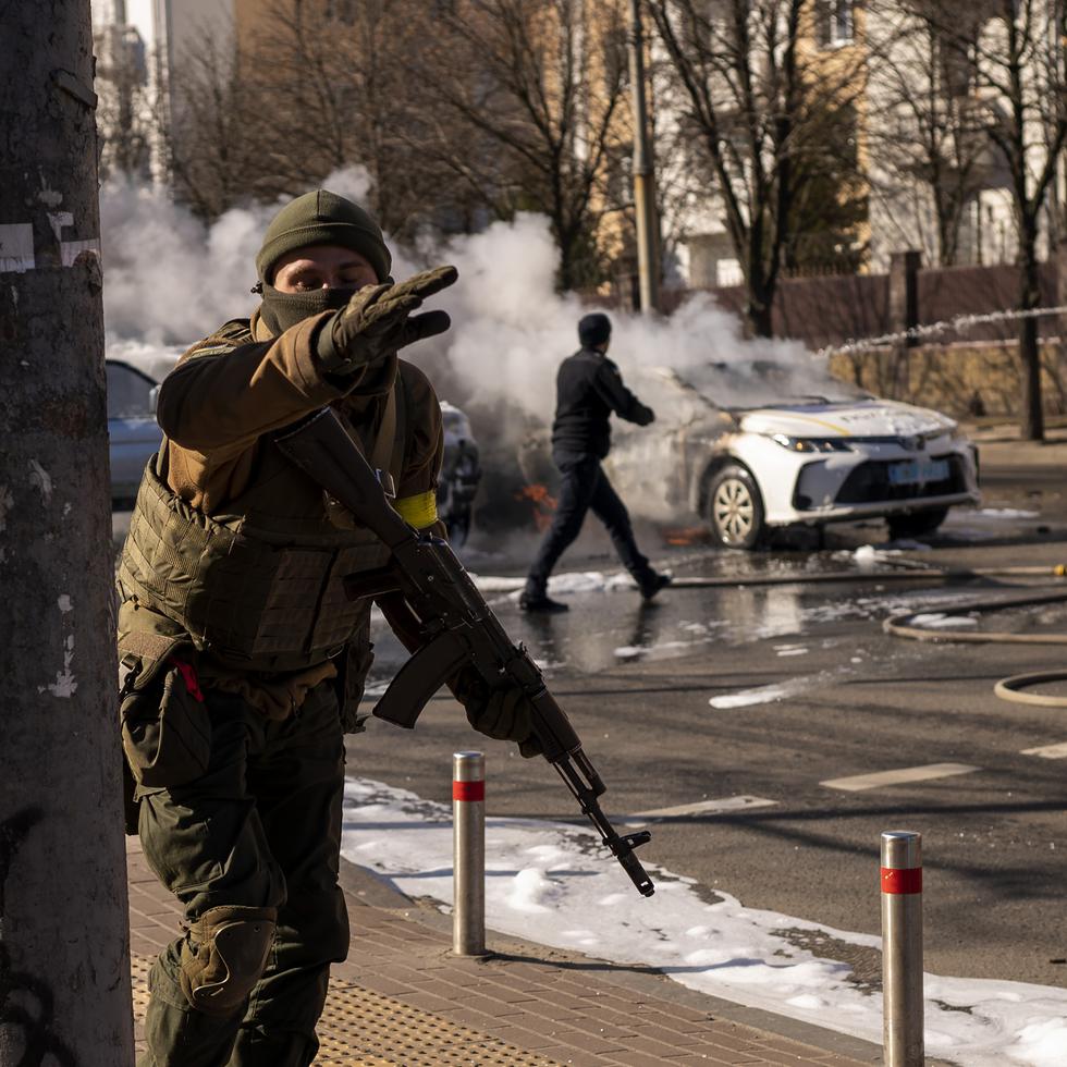 Soldados ucranianos toman posiciones en torno a una instalación militar mientras arden dos automóviles en una calle en Kiev.