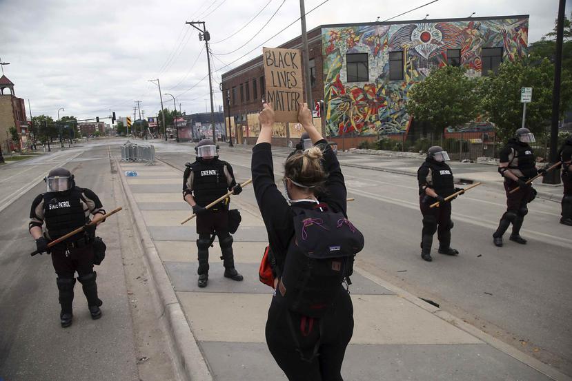 Una manifestante sostiene un letrero frente a agentes estatales de Minnesota que bloquean la avenida que conduce a la comisaría de Minneapolis. (AP)