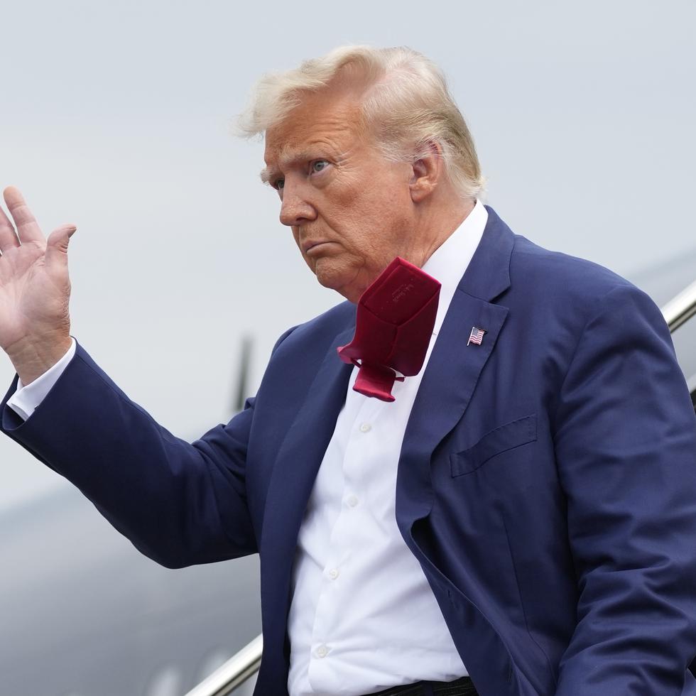 El expresidente Donald Trump saluda a los presentes mientras se baja de su avión.