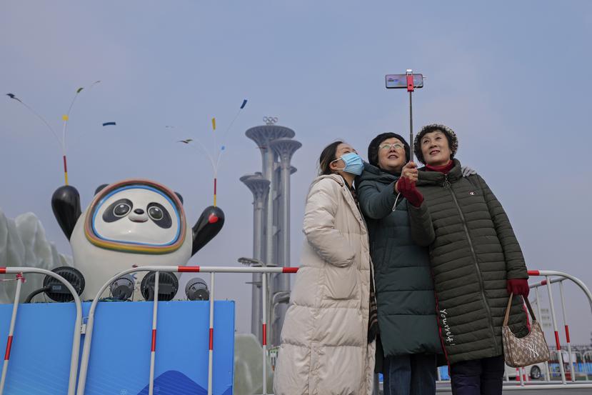 Una mujer porta una máscara mientras se toma una fotografía con otra personas frente a la mascota de los Juegos Olímpicos de Invierno de Pekín.
