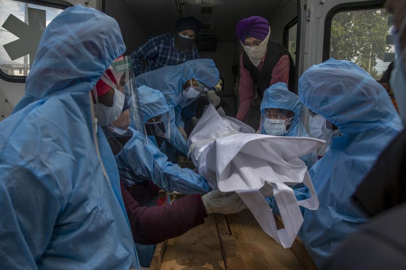Voluntarios retiran el cuerpo de un muerto por COVID-19 del interior de una ambulancia para cremarlo.